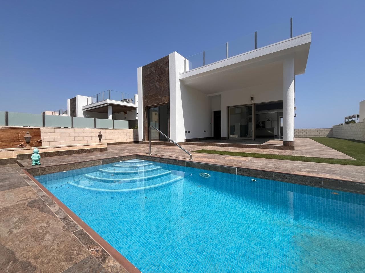Super modern detached villa for sale located in an exclusive residential complex in Villamartin, just minutes from the well known Villamartin Plaza and the huge variety of international restaurants, supermarkets and convenience stores. This Villa has been built to a high standard and offers the perfect blend of comfort and luxury. This villa sits on a 330m South facing, sunny plot with private swimming pool, off road parking and wraparound sun terraces which have been finished with artificial grass for comfort. Inside is a huge living area with impressive floor to ceiling windows and patio doors providing lots of natural light and lead directly outside to a relaxing covered terrace area overlooking the swimming pool. There is an uber modern fully equipped kitchen with an independent utility, laundry and storage room. The villa has a huge master bedroom with en-suite bathroom, two double guest bedrooms and a family bathroom complete with bathtub. This villa also boasts a superb rooftop solarium with very pretty views towards the neighbourhood and out towards Torrevieja pink lakes. Built on one level this property provides ample space for holiday or full time living and has been finished with many many extras including electric blinds throughout and ducted air-conditioning. The villa has just been painted externally and is sold unfurnished.