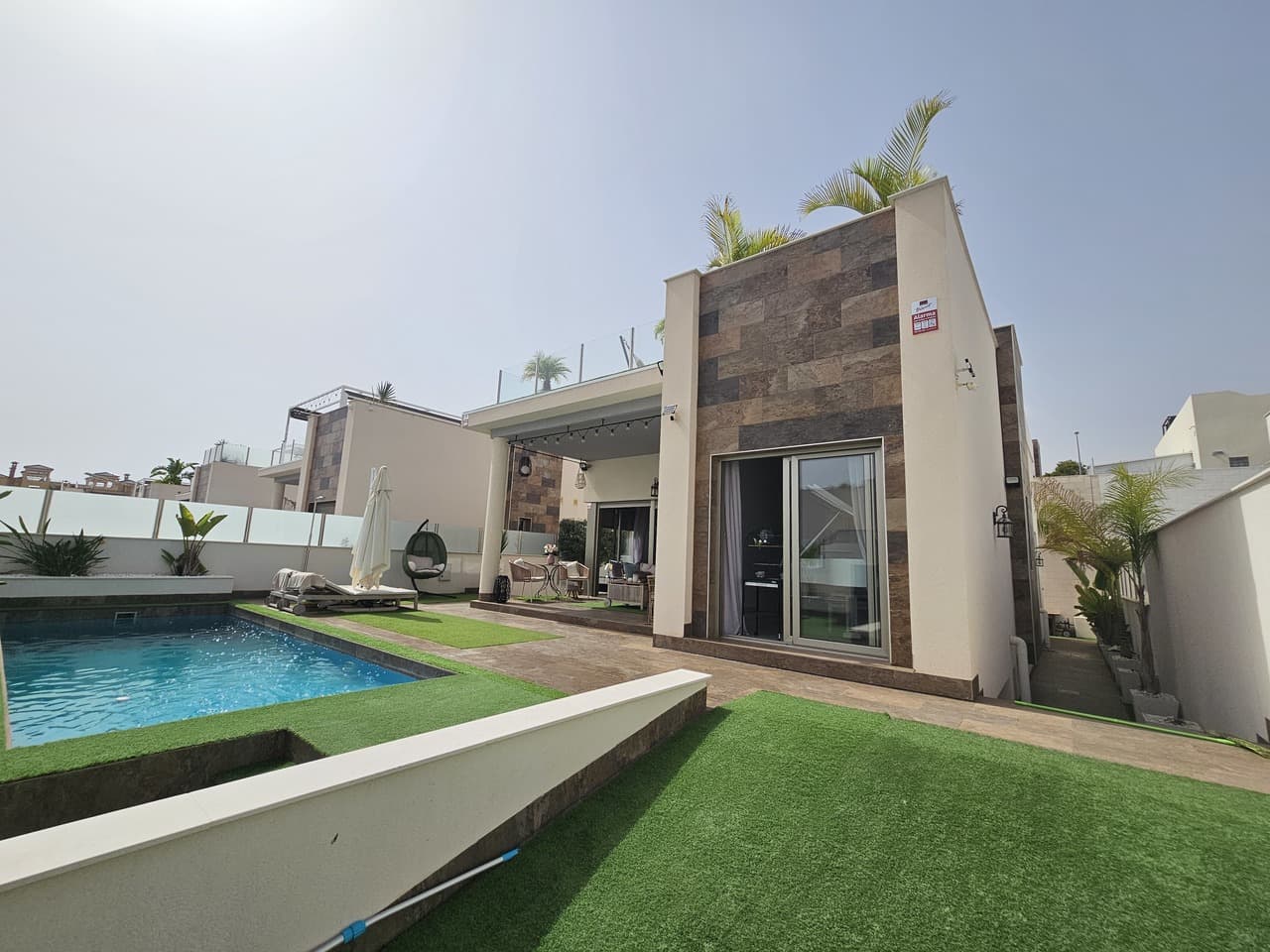 Immaculate and very well presented modern detached villa for sale located in an exclusive residential complex in Villamartin. This villa sits on a 329m sunny plot with private swimming pool, off road parking and wraparound sun terraces which have been finished with artificial grass for comfort and style. Inside the villa on the ground level you will find the huge open plan living room and sleek, stylish fully equipped kitchen, the master bedroom complete with en-suite bathroom along with two double guest bedroom and family bathroom. The villa has high ceilings and patio doors throughout providing lots of natural light leading directly outside to the covered terrace area overlooking the swimming pool and sun terrace. The villa also has a huge basement which provides the exact same footprint as above providing a second living room which is currently used as a gymnasium and games room, a super large bedroom with private lounge area and bathroom, the fifth bedroom, a additional family bathroom along with a laundry and utility room. The property also boasts a fabulous solarium with very pretty panoramic views towards the neighbourhood and out towards Torrevieja pink lakes and pine forest. This very useful space has a retractable sun awning to provide shade along with a private sun bathing area, electrical points, sink and water tap. This Villa has been built to a high standard and offers the perfect blend of comfort and luxury. It is sold fully furnished with many, many extras including electric blinds throughout, ducted air-conditioning, external solar lighting and private parking on the plot.