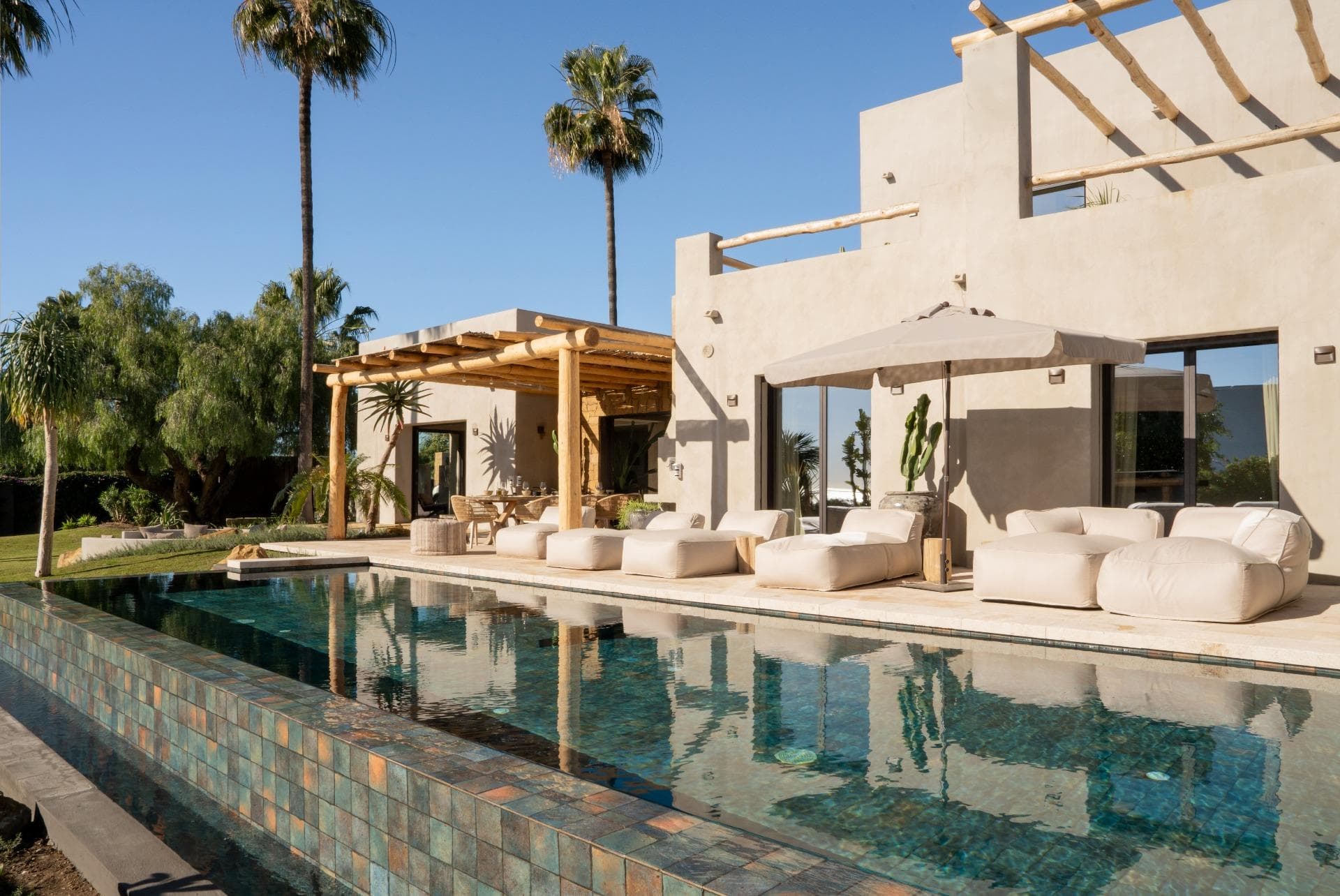 This unique villa, fully renovated in 2024, blends refined design influences from Mexico, Thailand, Ibiza, and Andalucía, creating a distinctive and relaxed atmosphere. Located in the emerging area of Selwo, the property enjoys beautiful sea views from the garden and pool level and a strong sense of privacy. The villa is arranged over two levels and offers five spacious en-suite bedrooms. The main living area features a cozy lounge with a working fireplace, seamlessly connected to a stylish open-plan kitchen and dining area, complemented by ample storage and a guest cloakroom. Outdoor living is a key highlight, with a heated infinity pool and poolside shower, a south-facing landscaped garden, multiple seating areas, a pétanque court, and an exotic pergola with a lounge corner. The main terrace is ideal for entertaining, featuring an Argentinian barbecue and an elegant dining area for al-fresco meals. The entire upper floor is dedicated to the master suite, offering a private open terrace with sun loungers and outdoor shower, a spacious dressing room, and a full bathroom with bathtub and walk-in shower. Finished with polished concrete floors throughout, the villa includes underfloor heating in all bathrooms, additional insulation, individual air conditioning units, ceiling fans, and 24 solar panels supplying hot water and heating the pool. Ideally located less than 1 km from the beach, within walking distance of restaurants and a padel tennis club, and just 10 minutes from Estepona and Puerto Banús, this architecturally distinctive home is truly incomparable on the coast.