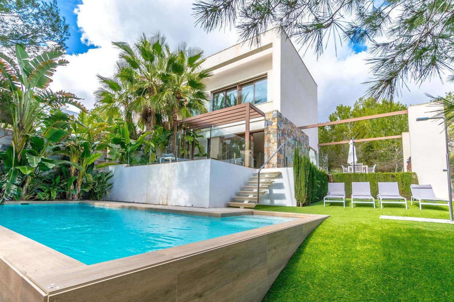 Semi-Detached Villa Acacia – Las Colinas Golf & Country Club Discover a unique blend of modern luxury and natural tranquility in this stunning south-facing semi-detached villa at Las Colinas Golf & Country Club. Situated at the very edge of a private, gated community, this home offers absolute privacy, breathtaking surroundings, and premium features for an exclusive living experience. Main Floor: A designer kitchen with high-end appliances, which can be elegantly concealed behind a sleek white wall. The spacious living area opens directly onto the outdoor dining space, sunbathing area, and private pool, creating a seamless indoor-outdoor flow. The master bedroom, complete with an en-suite bathroom, also enjoys direct access to the lush garden. A guest toilet adds convenience to this level. Upper Level: Two bright bedrooms, each with access to a balcony, a shared bathroom, and an additional private terrace to take in the peaceful surroundings. Lower Level: A large bedroom with an en-suite bathroom and a private patio. This floor also features a big fitted wardrobe and a spacious storage room beneath the staircase. The villa is perfectly integrated into its natural surroundings, with mature trees enhancing its serene atmosphere. A small putting green in the back courtyard provides a personal space for leisure and relaxation. With ample parking options, underfloor heating in all bathrooms, and a seamless blend of indoor and outdoor living, this home is an exceptional retreat within one of Spain’s most exclusive communities. Las Colinas Golf & Country Club A World Apart! Las Colinas Golf & Country Club is one of the most prestigious resorts on the Costa Blanca! It is an exclusive and unique 330 hectare golf resort with many sports facilities including golf, padel, hiking, fitness, yoga and much more. It is A World Apart where you can enjoy a healthy Mediterranean lifestyle. With an exceptional climate and first class services, the resort has been recognised as “Spain’s and Europe’s Leading Villa Resort” by the World Travel Awards in recent years. Nestled among the hills of the Dehesa de Campoamor – on the Mediterranean coast south of Alicante – Las Colinas Golf & Country Club is a unique natural area that has been carefully preserved and where exclusive homes have been integrated into the surroundings where you can relax and enjoy the scenery. This resort, with some excellent restaurants and the Wow Beach by Las Colinas has an international reputation and is well known and sought after by celebrities. Find your dream home today by taking a look at the most beautiful and exclusive homes we have to offer!