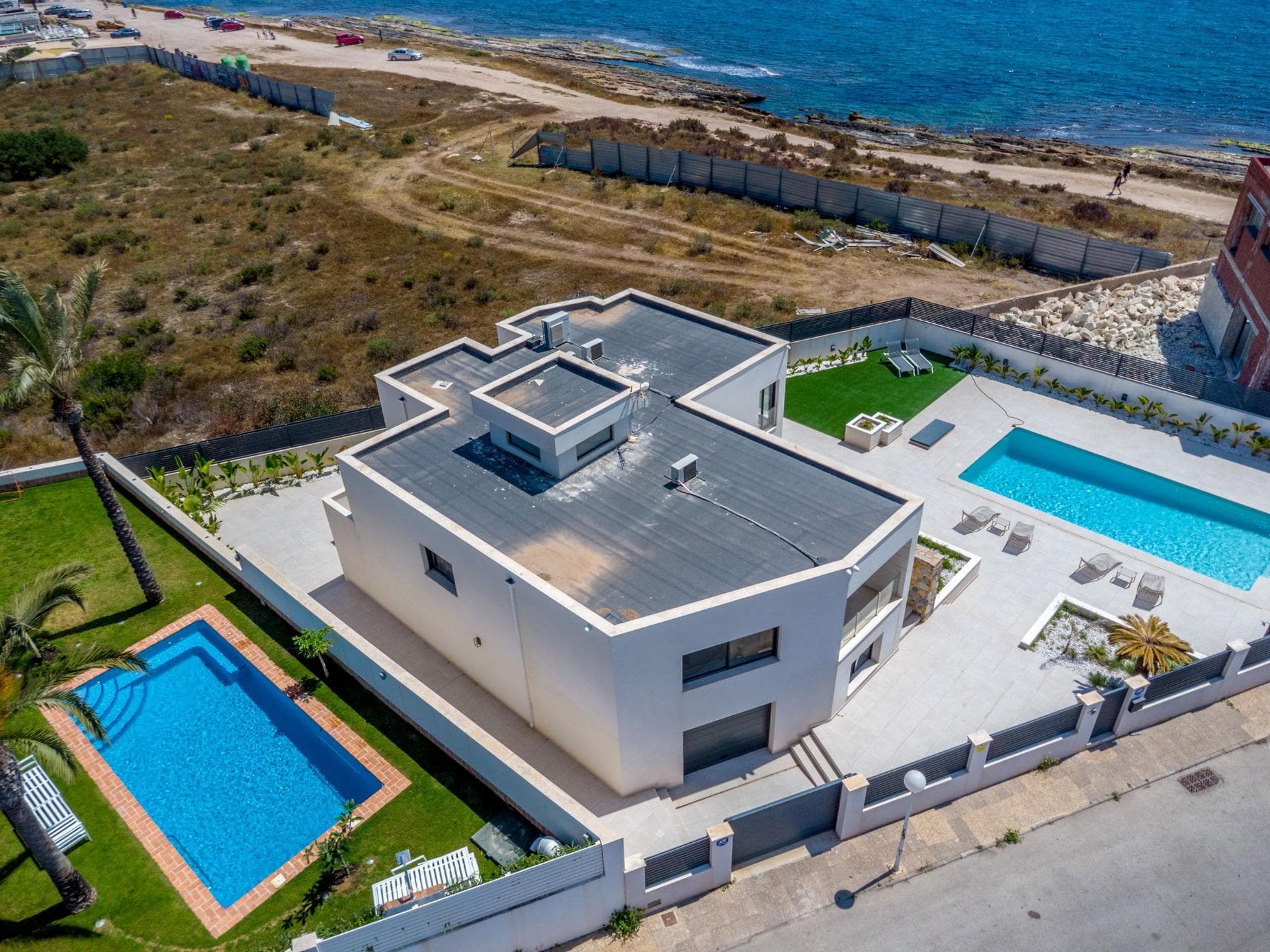 Step into luxury with this spectacular modern villa, located in one of the most prestigious and peaceful residential areas on the Costa Blanca. Designed with elegance, space, and Mediterranean lifestyle in mind, this stunning two-story home offers the ultimate comfort, privacy, and outdoor living. Set on a generous plot, the property boasts a sleek architectural design with clean lines, natural stone accents, and expansive windows that flood the interior with natural light. The beautifully landscaped garden features a lush green lawn, ideal for family activities, a mini football area, and multiple lounge zones. The highlight of the exterior is the sparkling private swimming pool surrounded by a sun-drenched terrace—perfect for relaxing, entertaining, or enjoying the sunny Spanish climate year-round. Inside, the villa features 5 spacious bedrooms and 3 elegant bathrooms, providing ample space for family and guests alike. The ground floor offers a bright, open-concept living area with modern finishes and direct access to the outdoor spaces, while the upper level enjoys tranquil views and large terrace—perfect for morning coffee or evening relaxation. The villa also includes a very large private garage, offering secure parking for multiple vehicles as well as generous storage space—an exceptional bonus rarely found in similar properties. The property has a high grade security system with motion detection and live/recording video feature which protects and monitors the inside and outside 24 hours a day, 7 days a week. The system is linked to local law enforcement and can be monitored via your smartphone or computer anywhere in the world, giving you peace of mind. Additional features include: - High-quality materials and finishes throughout  - Air conditioning and climate control  - Private onsite parking and gated access  - Fully fenced plot offering privacy and security  Located just minutes from the golden beaches of Orihuela Costa and the vibrant center of Torrevieja, this exquisite property is perfectly positioned close to international schools, golf courses, shopping centers, and fine dining—delivering a lifestyle of exclusivity, convenience, and relaxation. Whether you’re searching for a luxurious permanent residence, a stylish holiday retreat, or a high-potential investment, this extraordinary villa offers a rare opportunity in one of the Costa Blanca’s most coveted locations.