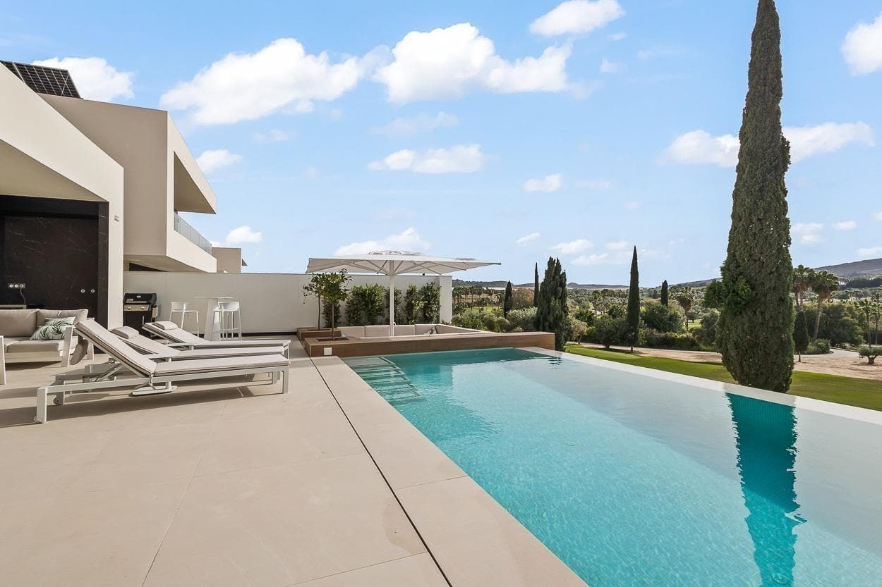Villa med 5 soverom og stor kjelleretasje på første linje til golfbanen til salgs i Algorfa. Et Moderne Mesterverk på Costa Blanca Opplev det beste av middelhavsliv med denne eksklusive nybygde villaen fra 2024, beliggende på første rad mot golfbanen i det prestisjefylte La Finca Golf Resort i Algorfa. Denne enestående eiendommen kombinerer moderne arkitektur med førsteklasses materialvalg, høy funksjonalitet og gjennomtenkte løsninger for komfort og tilgjengelighet. En bolig som balanserer stil, romslighet og ro, i hjertet av Sør-Spania. Hovedfunksjoner Førsteklasses beliggenhet ved golfbanen – Panoramautsikt over La Finca Golf 5 romslige doble soverom og 4 stilrene bad Separat gjesteleilighet med 3 soverom – Eget kjøkken og privat inngang Privat heis – Enkel tilgang til alle etasjer uten trapper Rullestolvennlig utforming – Brede ganger, trinnløse overganger og åpne flater Eksklusivt kjøkken – Fullt utstyrt med høykvalitets Siemens hvitevarer Vannbåren gulvvarme i hele boligen – Optimal komfort året rundt Smart hjem-automatisering – Styring av lys, persienner, klima og mer Privat infinity-basseng – Med elektrisk bassengdekke og avslappende loungeområde Pent opparbeidet middelhavshage – Elegant og lettstelt Underjordisk garasje med plass til 2 biler – Inkludert lagringsplass Høyhastighets internett – både inne og ute Avansert alarmsystem med videoovervåkning Planløsning og Design Villaen er elegant fordelt over to hovedetasjer: Hovedetasje: Åpen stue- og kjøkkenløsning, hovedsoverom med walk-in garderobe, ekstra soverom og utgang til bassengterrasse Underetasje: Fullverdig gjesteleilighet med 3 soverom, Siemens-kjøkken og egen inngang – ideell for familie, venner eller utleie Garasjenivå: Privat garasje for to biler, vaskerom og oppbevaringsplass Store vindusflater gir rikelig med naturlig lys og skaper en sømløs overgang mellom innendørs og utendørs oppholdsrom. Beliggenhet – La Finca Golf Resort, Algorfa Eiendommen ligger i den sjarmerende byen Algorfa, i det fruktbare området Vega Baja del Segura, omgitt av sitruslunder og tradisjonell spansk landsbyatmosfære. Samtidig gir La Finca Golf Resort tilgang til moderne fasiliteter og eksklusiv livsstil. På området: Supermarked, restauranter, barer, apotek og velværesenter Golf: 18-hulls mesterskapsbane med klubbhus og treningsområder Strender: 20 minutter til Guardamar del Segura og Torrevieja Shopping: Nær La Zenia Boulevard og Habaneras kjøpesentre Flyplasser: Alicante (40 minutter), Murcia internasjonale lufthavn (55 minutter) En Livsstil med Eleganse, Komfort og Tilgjengelighet Dette er mer enn en villa – det er en privat oase som tilbyr luksus, ro og funksjonalitet i perfekte omgivelser. Enten du ser etter en fast bolig, feriehus eller en trygg investering, gir denne eiendommen deg varig verdi og et tidløst middelhavsmiljø.