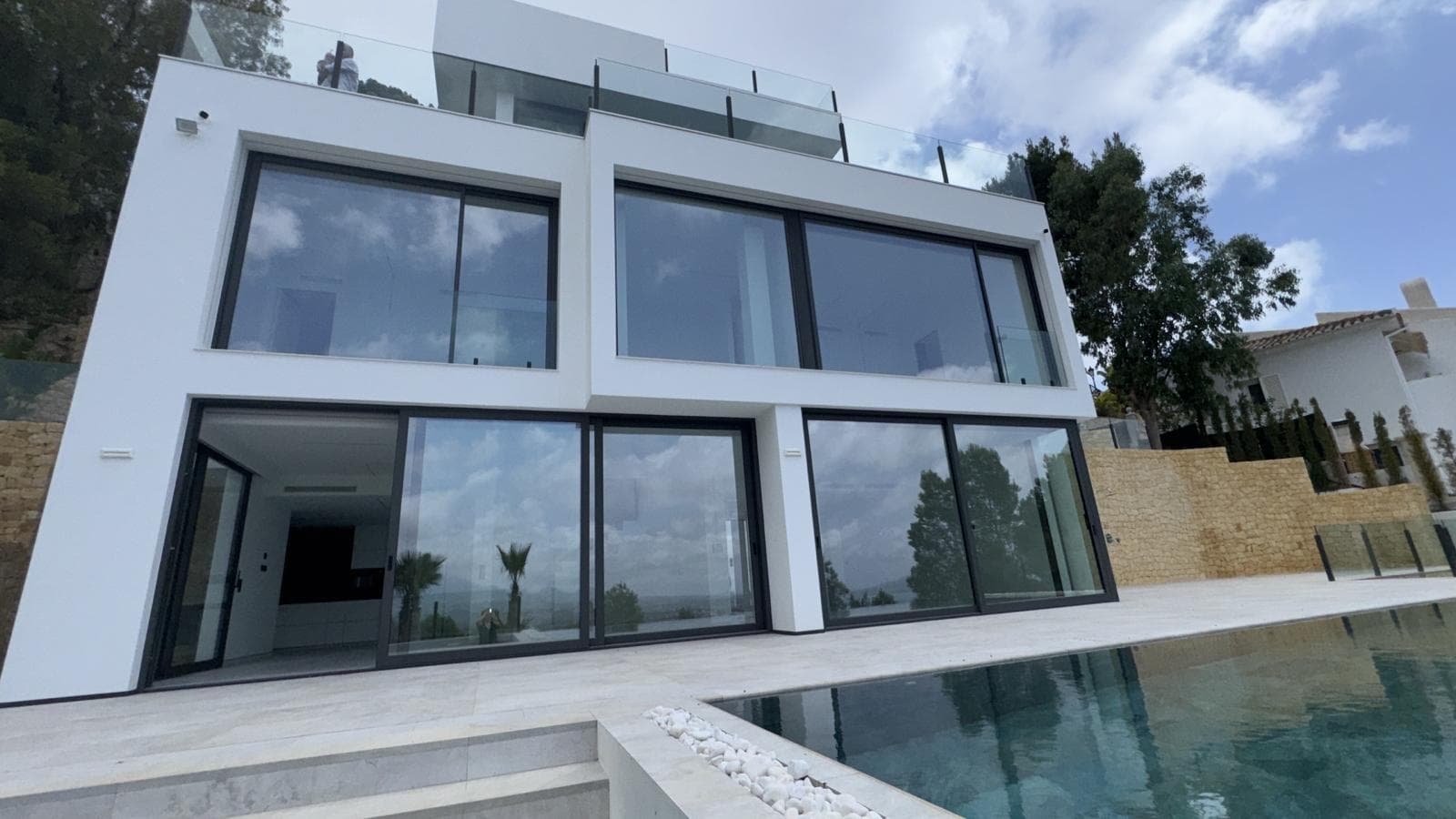 Una villa moderna con vistas panorámicas al mar y a la montaña, ubicada en una urbanización segura y prestigiosa - "Altea Hills", que es famosa por sus impresionantes vistas, impresionantes villas, así como paz y privacidad garantizadas. Al entrar en la parcela, encontrará un aparcamiento exterior para 2 coches, así como una amplia zona abierta con impresionantes vistas al mar y a las montañas. Bajando por las escaleras, accederá al nivel superior de la villa, junto a la entrada principal y al ascensor. A la izquierda de la entrada principal se encuentra un armario ropero para abrigos. En la planta siguiente hay 4 dormitorios, todos con baño en suite. Cada dormitorio dispone de espacio para un armario empotrado, mientras que el dormitorio principal cuenta con una estancia adicional que puede utilizarse como vestidor independiente o dormitorio infantil. El baño principal dispone tanto de ducha como de jacuzzi. En la planta más baja se encuentra un amplio salón con cocina y comedor de estilo abierto. Junto a la cocina hay un cuarto auxiliar, ideal para colocar la lavadora, un congelador y otros electrodomésticos. En este mismo nivel hay también un dormitorio de invitados y un aseo con ducha. Desde el salón se accede a una gran terraza con vistas panorámicas al mar y a las montañas, a la piscina tipo “infinity” y a la zona de barbacoa. Junto a la piscina hay una ducha exterior. La vivienda está equipada con sistema de aire acondicionado, calefacción por suelo radiante y sistema de “hogar inteligente”.