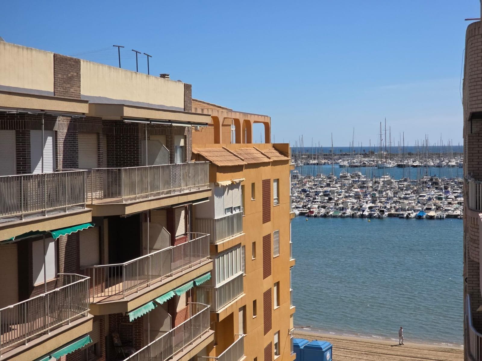 Descubra este magnífico apartamento semireformado ubicado en la cotizada zona de Acequion, en Torrevieja. Con una superficie generosa de 93 m², esta propiedad se encuentra a solo 50 metros del mar Mediterráneo, ofreciendo un estilo de vida costero inigualable. La vivienda cuenta con tres amplias habitaciones que garantizan el descanso y confort deseados. Su cocina equipada es ideal para los amantes del arte culinario, mientras que su luminoso salón se desliza hacia un encantador balcón desde donde disfrutar vistas al océano cada mañana. La orientación este-oeste permite aprovechar tanto el sol matutino como las suaves brisas vespertinas. Los acabados incluyen carpintería interior y exterior de aluminio combinando estética moderna con funcionalidad; además sus suelos acrílicos ofrecen elegancia junto a durabilidad. Este impresionante piso no solo destaca por sus características internas sino también por su ubicación privilegiada cerca de supermercados, centros comerciales y médicos así como colegios e instalaciones deportivas incluyendo campos de golf cercanos. Para aquellos aficionados al aire libre hay parques ideales para pasear o realizar actividades recreativas.