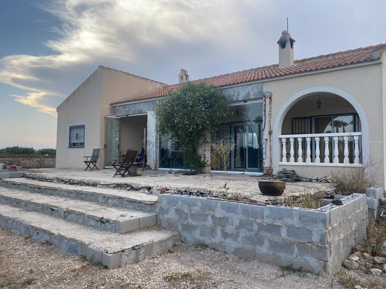 Today we present this fantastic 110 m2 house on a 2,500 m2 plot, located in the heart of the orchards of La Vega Baja del Segura, in the town of Benejuzar. The property consists of three bedrooms, two bathrooms, a gallery, a terrace, a fully equipped separate kitchen, and a parking area. The green areas feature several palm trees, fruit trees such as pomegranate, orange, lemon, fig, apple, and olive trees, and several tall plants. It has a self-consumption solar panel system and a regular Iberdrola electricity grid, allowing both to operate independently. The house is sold furnished and equipped. Contact us for more information.