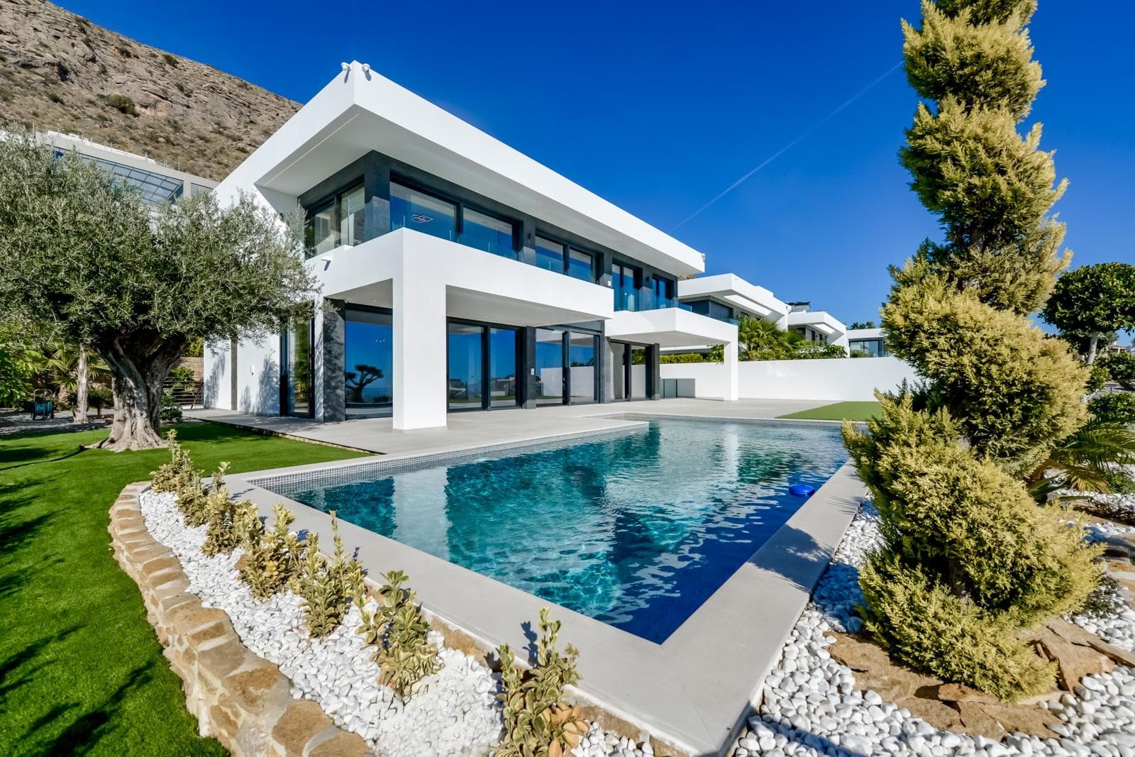 VILLA DE LUJO EN FINESTRAT CON VISTAS AL MAR

Villa de lujo de nueva construcción con vistas al mar en Sierra Cortina, Finestrat.

Llegando a la Urbanización hay un muro de piedra natural con una altura de 7 metros y las puertas automáticas de acceso al chalet llegando al garaje cubierto a nivel de calle con doble altura, luz natural y jardín con palmeras de diferentes alturas de 180 m2, una sala acristalada de 78 m2 con ascensor, escalera interior, guardarropa y espacio suficiente para poner sillones, convertir este espacio en un despacho o simplemente una sala de espera para visitas.

La siguiente planta de 190 m2 de espacio cerrado está situada por debajo del nivel de la parcela pero 3 metros por encima del nivel de la calle y por tanto con luz natural. Se puede acceder a ella por el ascensor o la escalera interior del chalet, o por la escalera exterior del garaje, en este último caso sólo se puede acceder a los pasillos exteriores, al cuarto de instalaciones o a la puerta principal de esta planta, realizando así el mantenimiento de la vivienda sin necesidad de entrar dentro de la casa. Dentro de esta planta encontraremos 4 amplios dormitorios, salón con patio inglés de 17 m2 con la escalera de acceso a la parcela, lavadero, 2 baños, pasillos exteriores de 40 m2 y cuarto de instalaciones.

Cuando subimos a la planta principal por 3 accesos vemos un salón de 130 m2 con doble luz, cocina abierta, aseo de invitados, vistas panorámicas al mar, y piscina de 54 m2 de laminado, un precioso jardín y 2 amplias terrazas cubiertas.

A la planta de dormitorios accedemos por ascensor o escalera interior donde veremos un Dormitorio Principal de más de 50 m2 con baño en-suite, vestidor y terraza, dos dormitorios de unos 20 m2 cada uno, un baño y la terraza para estos dormitorios.

Villa está equipada con Led exterior e interior, calefacción por suelo radiante, domótica, cristales Gamma de alta, aire acondicionado centralizado, persianas automáticas, techos altos y mucho más:
Salón- 95 m2
Dormitorios- 8 (principal 52 m2 y secundario 20 m2)
Baños- 5
Parcela- 890 м2
Construido- 998 м2
Piscina- 12 X 5
Cuatro Plantas
Jardín (20 m2) - totalmente terminado con sistema de riego automático
Ascensor (Otis) dentro de la casa
Calefacción por suelo radiante
Domótica (control de aire acondicionado, suelo radiante, iluminación interior y exterior, persianas)
Persianas eléctricas
Luces exteriores e interiores marca Siemens
Techos altos de hasta 3,20 m de altura
Impresionantes vistas al mar
Una planta para invitados
Calefacción aerotérmica
Cocina totalmente equipada con isla
Armarios empotrados
Suelo de gres porcelánico 
Pared con piedra natural tallada a mano
Garaje para 4 vehículos con puertas automáticas 160 m2 + hall de entrada 78 m2
Parking abierto 37

Chalet situado en el complejo Sierra Cortina, junto a dos campos de golf, parques temáticos, un gran centro comercial y a pocos minutos de las playas de Benidorm.

Finestrat situado en la comarca de la Marina Baixa de la Costa Blanca, cerca de la vecina Benidorm y a unos 40 kilómetros de la ciudad de Alicante y del aeropuerto internacional.

El pueblo está situado en la ladera del Puig Campana y ofrece hermosas vistas de las montañas, la costa y el mar Mediterráneo.