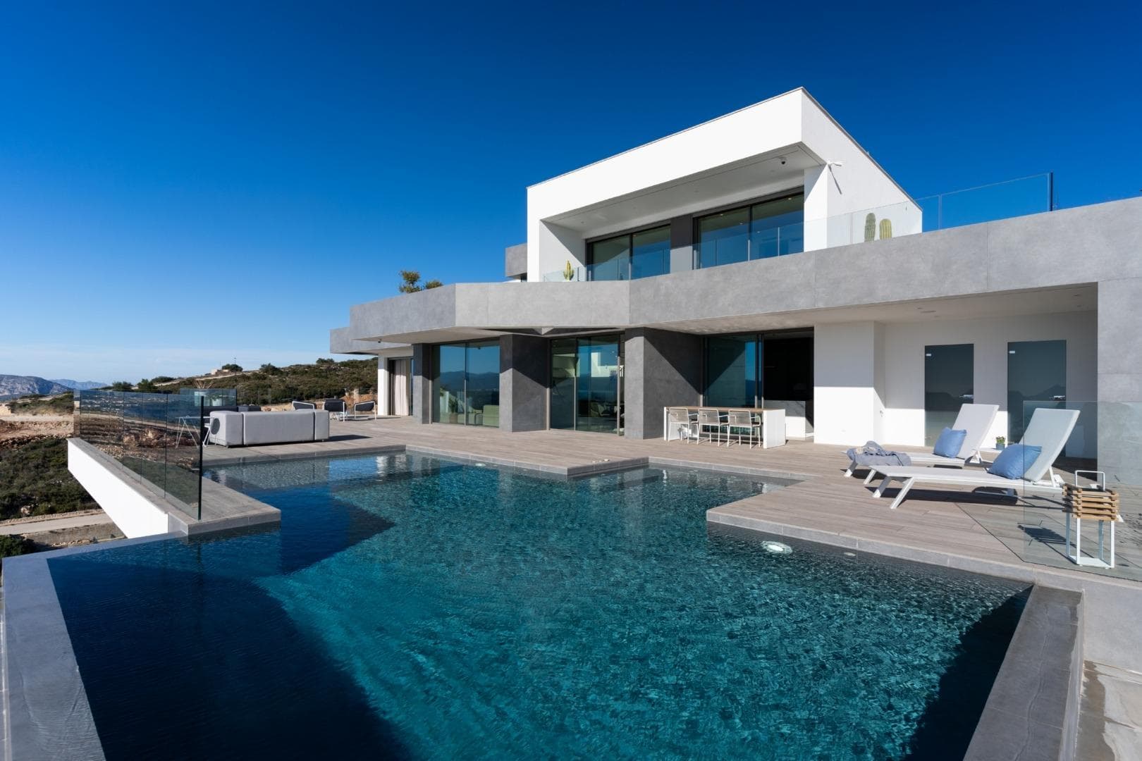 VILLA DE LUJO DE OBRA NUEVA EN CUMBRE DEL SOL

Villa emblemática de nueva construcción en Benitachell. Su diseño del siglo XXI se integra perfectamente en el exclusivo entorno de Residential Resort Cumbre del Sol. Está construida sobre una parcela de 1168m2, donde al estar orientada al suroeste se pueden ver y disfrutar de increíbles puestas de sol.

Todo en esta villa grita calidad y estilo, con un diseño inteligente que ofrece una práctica distribución de la villa que optimiza, aún más, sus excepcionales vistas al Mediterráneo.

Una vivienda con muchos espacios para disfrutar del descanso y la vida familiar frente al mar. Dispone de varias estancias conectadas entre sí para poder vivir diferentes momentos del día en distintos ambientes. Un comedor y una sala de estar, una cocina con una isla central donde poder disfrutar de un desayuno perfecto, y un gran porche de verano con barbacoa. Todas estas estancias están dispuestas para que puedas disfrutar de una buena conversación, celebrar eventos familiares importantes o para que simplemente te relajes contemplando el mar.

El dormitorio principal ha sido diseñado pensando en la comodidad y el relax. Es un espacio privado con un gran cuarto de baño en suite con bañera y ducha frente al mar. También dispone de un gran vestidor y acceso a una terraza privada.

Cumbre del Sol se encuentra en Benitachell en el corazón de la montaña de la Llorenca, al norte de la Costa Blanca. Se encuentra entre las dos ciudades costeras de Javea y Moraira y está rodeado de zonas protegidas excepcionales como el Parque Natural de La Granadella. Está muy cerca de maravillosas playas y calas y de ciudades como Denia, Calpe y Altea.
Tanto si disfruta de un par de días, unas vacaciones, una temporada o el año completo en nuestro resort de lujo en Benitachell, comprobará que Cumbre del Sol cumple todas sus expectativas.
Golfistas, buceadores, amantes de la naturaleza y buscadores de sol están a pocos minutos de las decenas de destinos paradisíacos de la Costa Blanca que rodean nuestra urbanización.