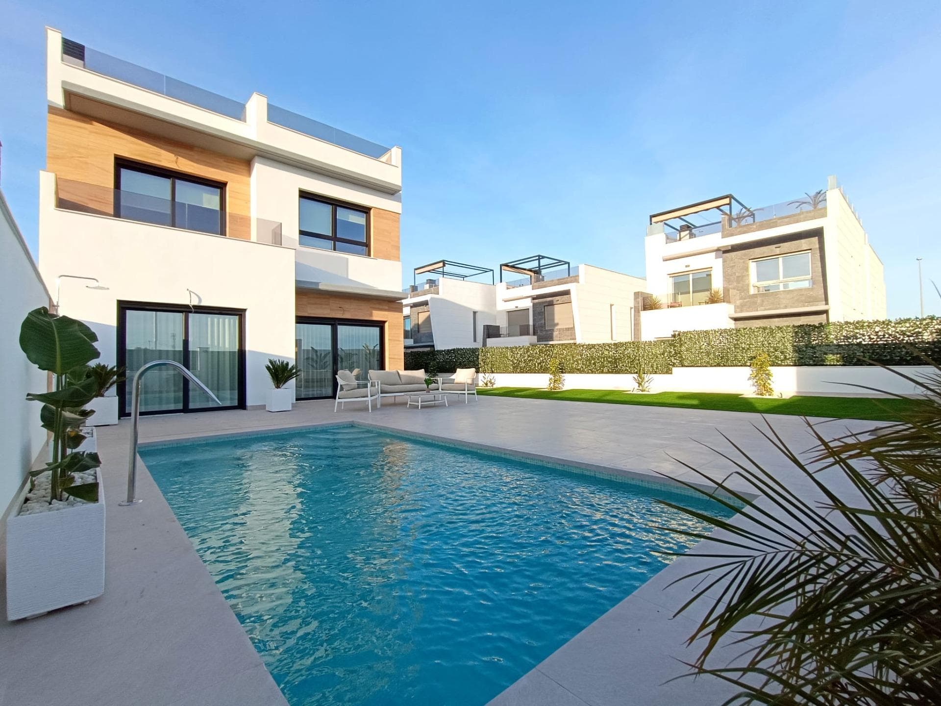 Luxury New Build Semi-Detached Villas in Benijófar, Costa Blanca

Prime Location in Benijófar with Convenient Access to Amenities

Discover a new level of luxury living in the charming town of Benijófar, a highly sought-after area on Spain’s Costa Blanca. These newly built semi-detached villas are situated in a vibrant neighborhood with a perfect blend of modernity and local charm, offering easy access to all essential services and attractions. Just 10 km from the golden beaches of Guardamar del Segura and 30 km from Alicante Airport, the villas are strategically positioned for convenience and lifestyle.

Spacious and Modern Design with Premium Finishes

Each villa is designed with a contemporary aesthetic, featuring clean lines and high-quality finishes. The layout includes three spacious bedrooms and three bathrooms, providing ample space for families or guests. The open-plan living-dining area seamlessly connects to a fully equipped kitchen, offering a perfect space for entertainment and family gatherings. Large windows allow plenty of natural light, creating a bright and welcoming atmosphere throughout the home.

Private Outdoor Spaces with Pool and Solarium

These villas include private outdoor spaces designed for relaxation and enjoyment of the Mediterranean climate. The tiled garden features a 2.5x5m swimming pool, perfect for cooling off on warm days, and ample parking space. The properties also come with a rooftop solarium, where you can enjoy views of the surrounding area. The solarium is equipped for a potential jacuzzi installation, making it a perfect spot to unwind and enjoy the sunset.

High-Quality Inclusions for Ultimate Comfort

Every villa comes fully equipped with top-of-the-line appliances, including a panelled fridge freezer, induction hob, panelled dishwasher, built-in microwave, and oven. Additional features include air conditioning units for climate control, underfloor heating in the bathrooms, and electric shutters for privacy. Spotlights and outdoor wall lights enhance the ambiance, making each villa both functional and luxurious.

Benijófar: A Blend of Tradition and Modern Living

Benijófar is a charming village with a welcoming atmosphere, known for its beautiful church, local shops, supermarkets, pharmacies, banks, and delightful restaurants. Nature lovers will appreciate the nearby natural park, ideal for walking and exploring. Golf enthusiasts will find several golf courses within a short drive, while families can enjoy nearby water parks in Rojales (4 km) and Torrevieja (12 km). The villas are also well-connected, with the N-332 and AP-7 highways providing easy access to surrounding towns.

Ready to Make Benijófar Your New Home?

Embrace the luxury and convenience of these modern villas in Benijófar. Don’t miss this opportunity to enjoy life on the Costa Blanca. Contact us today to arrange a viewing and take the first step toward your dream home.