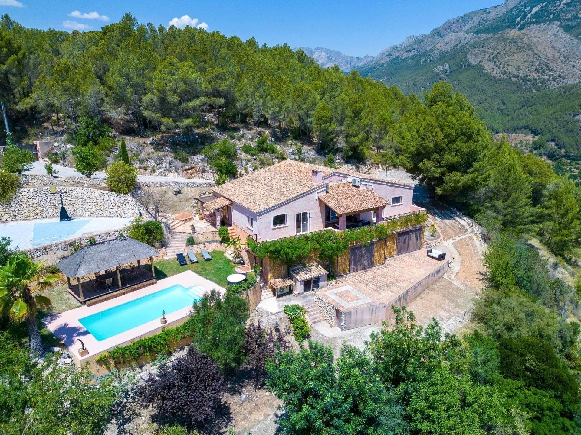 This spectacular villa is presented for sale, offering breathtaking panoramic views of the sea and the mountains, framed by an environment of pure nature. With a built area of 370 m² on a spacious plot of 19,900 m², the property ensures absolute privacy and a serene atmosphere, with paved access almost in its entirety (only 300 m of dirt road). The house is a former country estate (masía) completely rebuilt in 2007, preserving the charm of traditional stone-wall architecture while combining it with the comfort and design of a modern home. Its spacious, bright, and carefully decorated rooms convey freshness, elegance, and harmony. The villa is arranged over two levels, adapted to the natural slope of the land: Main floor: An elegant entrance hall welcomes you and leads to a large living-dining room, open to a designer kitchen with a central island. It features two en-suite bedrooms, one of them with a walk-in closet. All rooms have direct access to a spacious terrace with spectacular views. Ceramic floors and antique hydraulic tiles add character and authenticity. Lower floor: An independent area dedicated to the master bedroom, with a unique designer bathroom (stone sinks, hammam, automatic WC, and Italian bathtub), a luxury walk-in closet, private lounge, and an office —currently used as a music and recording studio— with its own bathroom. Large windows connect this level to the outdoors and its magnificent views. Solid oak flooring adds warmth and distinction. The outdoor spaces are designed to fully enjoy the climate and nature: large parking areas, several terraces, a heated private pool with open views, a chill-out area with a Bale for yoga or meditation, and a basketball court. Programmable outdoor lighting, automatic irrigation, and a large water tank complete the property’s comfort. The house is equipped with oil-fired underfloor heating, as well as two high-power air conditioning systems (hot/cold with anti-humidity function), ensuring comfort all year round. This villa is much more than a home: it is a retreat of peace, privacy, and natural beauty. Perfectly integrated into its surroundings, it is ideal both as a permanent residence and as an exclusive investment in one of the most privileged areas of the region.