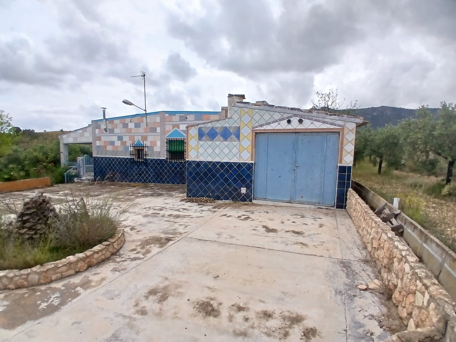 If you love peace and quiet and nature this is the place for you. The property has a good size living room with fireplace, a kitchen of 6.07m2 and 5 bedrooms of 7.46m2, 10.92m2, 9.31m2, 8.88m2 and 9.12m2, there is also a small bathroom of 3.47m2, with toilet, sink and bidet. Outside you will find another bathroom with shower of 4m2.Outside is a porch of 12.62m2 where you can enjoy the views of the garden and the mountains. There is also a pool of 19.25m2 and there are 2 garages, 1 next to the house of 22.76m2 and one behind the property of 12.09m2. Furthermore there is a barbeque area of 10.85m2.

The windows all have single glass, mosquito nets and wooden shutters.

The structure of the house is in good condition, there are no moist problems. However the whole house needs to be repainted and the bathroom and kitchen need updating. 

The house has no electricity, it has been used as a holiday home and they have one old solar panel for light, the kitchen is all on gas, including the fridge. A new solar installation is required. They have 2 water deposits, one to collect the rain water and another to be filled with drinking water by a truck. 

The large plot of almost 4.000m2 has several olive trees, as well as almonds, figs, mispel and grapes.

This remote country property is located on 9km from Yecla and has a 2 km long non-asphalted access road. Even though it is remote there is still 4G reception and there are a few neighbors around.