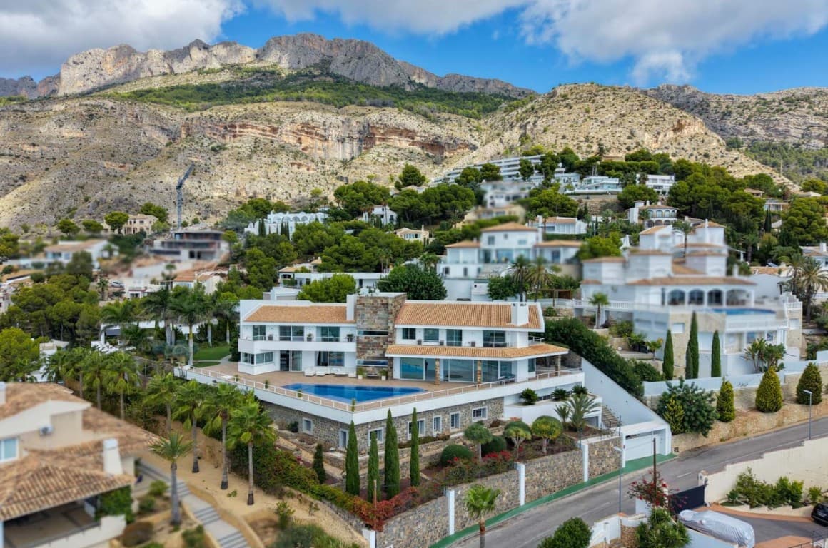 Esta impresionante villa es una obra de arte de la arquitectura moderna, ubicada en la prestigiosa Sierra de Altea, una de las zonas residenciales más exclusivas de la Costa Blanca. La propiedad se asienta sobre una generosa parcela de 2.035 m² y ofrece una impresionante superficie habitable cubierta de 1.605 m², distribuida en tres plantas, todas con ascensor y aparcamiento subterráneo adicional para seis vehículos. Diseñada para combinar el encanto mediterráneo con líneas limpias y contemporáneas, la villa encarna la elegancia refinada, la funcionalidad y el máximo confort.Desde su privilegiada ubicación, la villa disfruta de una panorámica de 360 grados que abarca el mar Mediterráneo al sur y la escarpada Sierra Bernia al norte. En días despejados, las islas de Ibiza y Formentera se vislumbran en el horizonte. A pesar de su tranquila ubicación, la propiedad se encuentra a poca distancia del centro histórico de Altea, las playas de arena y el puerto deportivo, así como de los clubes de golf y tenis, todos a pocos minutos.Los espacios principales están concebidos tanto para el entretenimiento a lo grande como para la intimidad familiar. Amplios salones, comedores y una cocina de diseño italiano de vanguardia con isla central se abren a una amplia terraza de más de 370 m². La sensación de amplitud se ve reforzada por los ventanales de suelo a techo que inundan de luz los interiores y enmarcan las espectaculares vistas al mar. La villa alberga un total de siete dormitorios y seis baños en suite, además de un aseo de invitados y un baño independiente, ofreciendo un amplio espacio para la familia y los invitados. Cada suite está diseñada individualmente para la comodidad y la privacidad, mientras que la opulenta suite principal ocupa todo el ala este de la primera planta. Este remanso de privacidad cuenta con amplios ventanales, una chimenea de bioetanol, dos terrazas con vistas al Mediterráneo, un suntuoso baño con bañera profunda y ducha de cristal, y un amplio vestidor.La planta baja de la villa está dedicada al ocio y el bienestar. La planta de recreo, de más de 500 m², está preparada para incluir una zona de cine, billar, sala de juegos, un gimnasio totalmente equipado, una sala de masajes, una sala de estar y relajación, y un spa con sauna, hammam y cueva de sal. Actualmente solo hay un gimnasio, pero los planos muestran la posibilidad de convertir esta planta en un auténtico paraíso de ocio. Debajo, el sótano alberga el garaje para seis coches, plazas para motos, trasteros y las instalaciones técnicas de la propiedad.En toda la villa se han seleccionado exclusivamente materiales y acabados de la más alta calidad. Mármoles cuidadosamente seleccionados, granitos exóticos y maderas nobles crean una atmósfera única de sofisticación. El equipamiento incluye aire acondicionado y calefacción Daikin, calefacción por suelo radiante, internet de fibra óptica de alta velocidad, sistemas de videovigilancia y alarma, así como domótica con control remoto desde cualquier dispositivo. Ventanas de doble acristalamiento con persianas automáticas, parqué y cerámica italianos, iluminación de diseño y cocinas a medida de Dada Molteni/Armani y Schüller, equipadas con electrodomésticos de alta gama Miele y Bosch, reflejan un lujo absoluto.Los espacios exteriores son igualmente impresionantes. Una terraza de madera conduce a la piscina infinita, enmarcada por un jardín subtropical perfectamente cuidado con jazmines, buganvillas, rosas silvestres, árboles frutales exóticos y elegantes palmeras. Un sistema de riego automatizado, iluminación ecológica y un sistema de cuidado del césped automatizado garantizan un mantenimiento sencillo. Un césped central de 400 m² integra una zona de meditación, una zona de barbacoa y la terraza de la piscina, ofreciendo múltiples ambientes para disfrutar del estilo de vida mediterráneo durante todo el año.Esta villa única es más que una residencia; es una propiedad excepcional concebida para quienes valoran la privacidad, la excelencia en el diseño y el máximo confort. Con sus imponentes vistas, su arquitectura innovadora y sus lujosos detalles, esta propiedad representa una de las mejores opciones disponibles actualmente en la Costa Blanca.