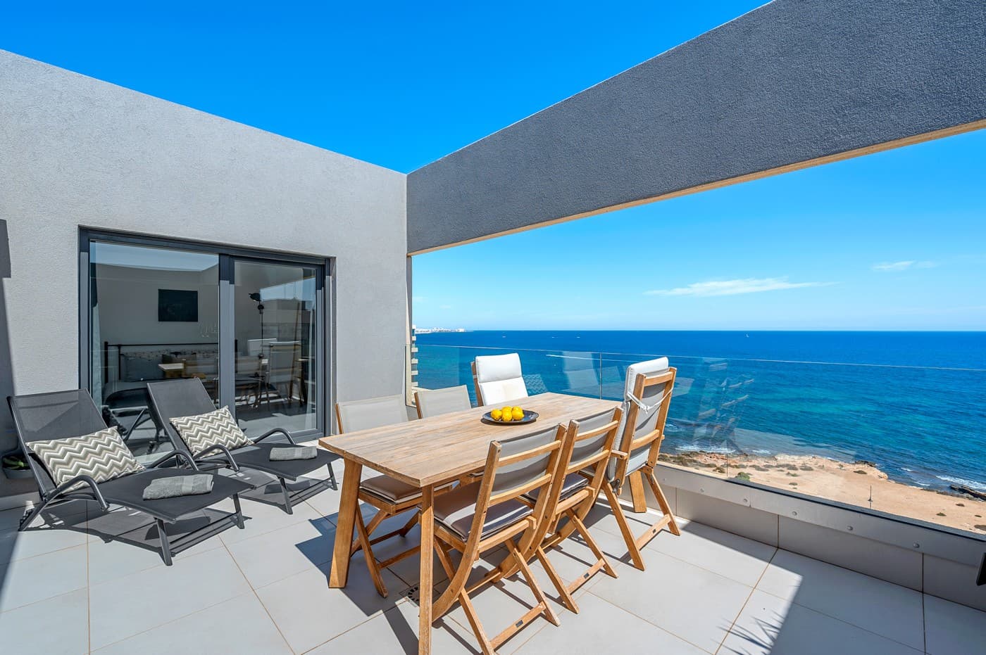 We are proud to present this stunning frontline beach penthouse, located on the top floor with spectacular, unobstructed views of the Mediterranean Sea. From here, you can enjoy a truly privileged perspective of some of the most beautiful parts of Spain. The beach lies just at your doorstep, while services, restaurants, and shops are only a short stroll away.

The apartment features two spacious bedrooms and two bathrooms, as well as an open-plan kitchen and living room, decorated in soft, harmonious tones. All interiors and installations are designed with high-quality materials, reflecting a refined Nordic style.

The entrance leads directly into the heart of the home: a bright, combined kitchen and living room with light flowing in from both sides of the building. The kitchen is fully equipped with everything you need—whether you are preparing a romantic dinner for two or entertaining friends and family. From the living room, you step out onto a generous east-facing terrace with unbeatable sea views, perfect for social gatherings, sunbathing, or simply enjoying the soothing sound of the waves in complete privacy.

The property also includes a west-facing balcony, where you can admire the sunset with a cup of tea and your favorite book. Thanks to the glazed façade, this space can also be enjoyed comfortably during the cooler winter months.

Both bedrooms benefit from large windows and direct access to natural light, with integrated wardrobes providing ample storage. Additional practical features include a utility space with a washing machine, a dedicated home office area, and a private garage with a wide parking space and a large storage room, conveniently located next to the elevator for easy access.

The apartment is sold fully furnished with tasteful, high-quality furniture, featuring elegant wooden details. Within the residential community, you will also enjoy several swimming pools (one of them heated), a padel court, and a summer snack bar by the pool area.

The current owners shared what they love most about living here:





“Waking up every morning to this dream view, with light pouring in and a coffee in hand while watching the sunrise—it feels unreal.”





“In the evenings we enjoy dinner on the west-facing terrace, watching the sunset and closing the glass doors if it gets chilly.”





“Sunshine all day—when it leaves one terrace, it shines on the other.”





“The large storage and parking, located right by the elevator, make life so practical—especially when loading groceries, golf clubs, or beach gear.”





“The privacy—no one overlooks the apartment. It’s wonderfully secluded.”





“It is incredibly quiet, except for the gentle sound of the waves if you open the windows.”





“Most of all, we feel safe, comfortable, and privileged living here.”





Punta Prima—just south of Torrevieja in Alicante—is one of the most sought-after areas on the Costa Blanca, offering a unique lifestyle with elegant promenades, crystal-clear waters, and immaculate beaches. The neighborhood boasts first-class restaurants, exclusive homes with modern architecture, and panoramic sea views. With year-round sunshine, prestigious golf courses nearby, excellent shopping, and Alicante International Airport only a short transfer away, Punta Prima combines relaxation, comfort, and luxury in perfect harmony.

This is a rare opportunity. Contact us today to arrange a private viewing.

Welcome!
