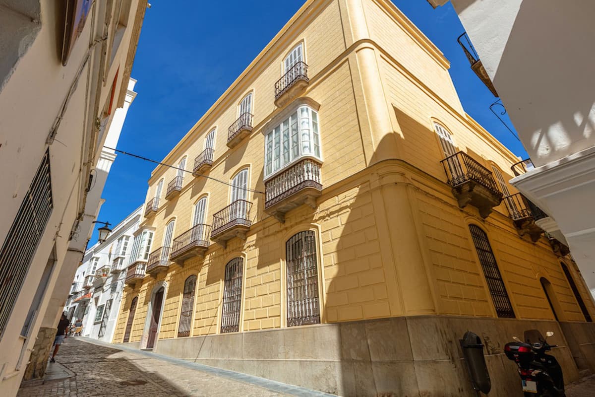 Bienvenidos a una joya histórica en el corazón del casco antiguo de Tarifa. Este majestuoso chalet independiente del siglo XIX, construido en 1850, ofrece una oportunidad única para inversores visionarios. Con 1.081 m² construidos, esta propiedad se distribuye en tres plantas y cuenta con 20 dormitorios y 4 baños, lo que la hace ideal tanto para uso residencial como para un proyecto turístico-comercial. La planta principal te recibe con un elegante vestíbulo, varios salones, almacenes y zonas que pueden ser transformadas según tus necesidades. La primera planta alberga un amplio salón, comedor, despacho, cocina y dormitorios, además de un encantador patio interior que ilumina el espacio con luz natural. La planta superior dispone de baños, dormitorios dobles, aseos, una zona de lavandería y una impresionante terraza con vistas panorámicas del casco antiguo y el puerto. El inmueble destaca por sus calidades de lujo para su época original, con suelos de mármol y baldosas hidráulicas, altos techos y detalles arquitectónicos como azulejos y cerrajería de época. Además, cuenta con un gran patio central con galerías y otros patios más pequeños que aportan luz y ventilación al interior del edificio. La orientación sur y este garantiza una excelente iluminación natural durante todo el día. Aunque la propiedad no dispone de calefacción, su estructura y diseño permiten una temperatura agradable durante todo el año. No pierdas la oportunidad de adquirir esta pieza única de la historia de Tarifa. Contacta con nosotros para más información y para organizar una visita. ¡Tu sueño de vivir o invertir en una propiedad con carácter y potencial está a un paso de hacerse realidad!