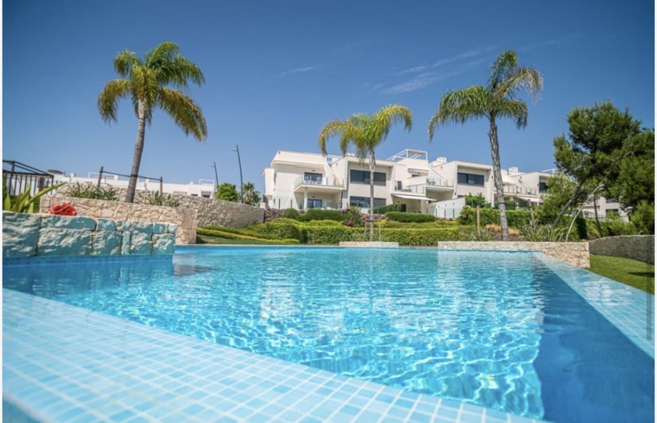 Welcome to this exceptional ground floor apartment with 2 bedrooms, where elegance, comfort, and design converge. From the spacious terrace, you will enjoy breathtaking panoramic views over the beautiful Lo Romero golf course, a place where every day feels like a vacation.This modern apartment, completed in early 2025, combines modern architecture with refined finishes. The open plan kitchen with integrated appliances exudes class thanks to its sleek matte white fronts and thoughtful layout, the ideal place to cook and enjoy.The two luxurious bathrooms are true gems of comfort, equipped with a stylish vanity, mirror, toilet, and a spacious walk-in rain shower. The master bedroom is an oasis of tranquility with a private en-suite bathroom – your personal spa, every day.Throughout the apartment, LED lighting and air conditioning with heating function ensure a pleasant indoor climate year-round. Outside, your private parking space awaits, securely located within the gated residence.This beautiful residence offers everything for carefree living: a spacious communal pool surrounded by an inviting lawn – the perfect place to relax and enjoy the Mediterranean sun. A unique apartment in a prime location, where living becomes pure enjoyment.