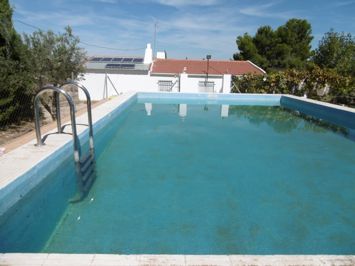 Encantadora villa situada a sólo 10 kilómetros de Yecla. Es una propiedad práctica y bien mantenida con tres dormitorios, una cocina funcional, un acogedor comedor con chimenea y un baño estándar. El espacio exterior es perfecto para el relax y el entretenimiento, con un amplio porche, una zona de barbacoa con cocina propia y chimenea, y un garaje y trastero. Una de las principales atracciones de la propiedad es la piscina vallada de 70.000 litros, que ofrece mucho espacio para el ocio y la diversión. La propiedad también cuenta con agua de riego, lo que facilita mantener verde y próspera la parcela de 5400 m2. Aquí encontrarás varios árboles frutales plantados, como olivos, melocotoneros, higueras, manzanos, perales, cerezos y vides. La villa está equipada con paneles solares y un generador, lo que garantiza un suministro constante de electricidad, incluso en este entorno rústico. Con la propiedad rodeada de naturaleza, podrá disfrutar de unas fantásticas vistas del sereno paisaje. Tenemos una gran cartera de propiedades en las zonas de la Costa Blanca y Costa Cálida, especializándonos en propiedades de campo, villas, fincas, solares edificables y opciones de diseño y construcción en las regiones de Alicante y Murcia con especial énfasis en Elda, Monovar, Pinoso, Sax. , Villena, Aspe, Fortuna, Albacete y muchas más zonas de los alrededores. Nos establecimos desde 2004 y contamos con décadas de experiencia en el equipo que aportamos para ayudarlo a encontrar y asegurar la nueva casa de sus sueños. Te ayudamos en cada paso del camino para asegurarnos de que tu compra en España sea segura y sin complicaciones. No estamos aquí para venderle una propiedad, estamos aquí para ayudarlo a realizar su sueño y encontrar lo que es adecuado para usted. Con nosotros estás en las manos más seguras. Contáctanos ahora para conversar sin compromiso sobre cómo tú también puedes hacer realidad tus sueños.