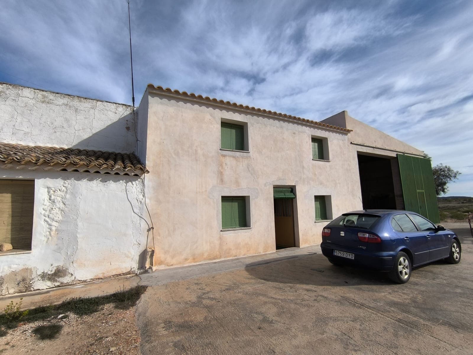 Casa adosada ubicada en la pintoresca zona rural de Yecla. Rodeada de almendros y olivos, esta propiedad tiene una superficie construida de 386 m², de los cuales 258 m² son para uso residencial. La vivienda se distribuye en dos plantas, con siete amplios dormitorios, un salón con una gran chimenea tradicional, cocina, despensa y un baño. Además de la superficie habitable, la propiedad ofrece amplios garajes y trasteros, un patio y cocheras compartidas con la casa adosada vecina. Para su beneficio y para sus actividades agrícolas, dispone de un viñedo de 7.300 m², con sistema de riego y en plena producción. Aunque la casa no tiene conexión a la red eléctrica, cuenta con cableado eléctrico funcional y acceso al agua de riego. Las renovaciones recientes incluyen un nuevo techo, fachada y algunas ventanas, aunque la mayoría de las habitaciones necesitan reformas. La casa se vende amueblada, pero tenga en cuenta que la maquinaria agrícola no está incluida en la venta. Sobre la zona: Yecla, ubicada en la Región de Murcia, es conocida por su pintoresco paisaje, sus viñedos históricos y su acogedora comunidad. A poca distancia del centro, esta propiedad disfruta de la tranquilidad rural, a la vez que se encuentra cerca de servicios esenciales como tiendas, restaurantes y colegios. Con su pintoresco entorno y su vibrante cultura local, Yecla es un lugar ideal para quienes buscan un estilo de vida tranquilo o una rentable actividad agrícola o turística. Sobre nosotros: Contamos con una amplia cartera de propiedades en la Costa Blanca y la Costa Cálida, especializándonos en fincas, villas, fincas, terrenos edificables y opciones de diseño y construcción en las regiones de Alicante y Murcia, con especial énfasis en Elda, Monóvar, Pinoso, Sax, Villena, Aspe, Fortuna, Albacete y muchas otras zonas de los alrededores. Llevamos establecidos desde 2004 y nuestro equipo cuenta con décadas de experiencia para ayudarle a encontrar y asegurar la casa de sus sueños. Le acompañamos en cada paso del proceso para garantizar que su compra en España sea segura y sin complicaciones. No estamos aquí para venderle una propiedad, sino para ayudarle a hacer realidad su sueño y encontrar la propiedad perfecta para usted. Con nosotros, está en las mejores manos. Contáctenos ahora para hablar sin compromiso sobre cómo usted también puede hacer realidad sus sueños.