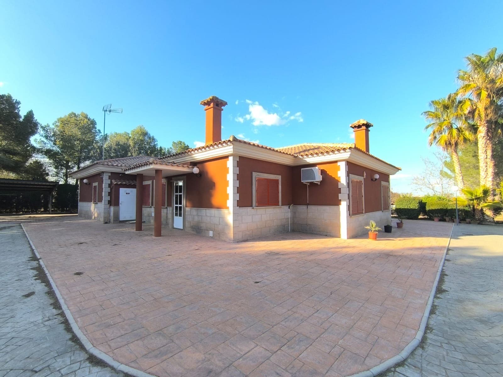 Descubra esta hermosa villa ubicada en una tranquila zona residencial, a solo 4 km de Yecla, con fácil acceso a tiendas, colegios y bares. Esta excepcional propiedad consta de dos casas modernas construidas con materiales de alta calidad, que ofrecen comodidad y estilo. La villa principal (construida en 2002) cuenta con: 5 habitaciones 2 baños Un acogedor salón completo con chimenea. Una cocina contemporánea Un gran solárium Amplios trasteros Interiores completamente amueblados y diseñados con estilo. Aislamiento térmico para eficiencia energética y calefacción y aire acondicionado centrales para comodidad durante todo el año. Segunda Casa (construida en 2015) incluye: Un generoso garaje equipado con tres puertas eléctricas, que sirve como gimnasio. Un anexo para invitados con baño accesible para sillas de ruedas. Características exteriores : el exterior de la propiedad está bellamente sombreado por árboles maduros e incluye: Una piscina cubierta de 10 x 4 metros, equipada con sistema de filtración, ideal para relajarse o entretenerse. Un jardín bien cuidado de 5600 m², perfecto para el ocio o el cultivo de plantas. Una cochera cubierta Un patio espacioso Las comodidades adicionales incluyen: Un sistema de limpieza de aguas residuales que apoya el riego de árboles Agua de riego de red y un tanque de agua potable Tanto la red eléctrica como un sistema de paneles solares de 2 kW Un sistema de alarma conectado a la comisaría para mayor seguridad. Esta hermosa, moderna y elegante casa está lista para mudarse. ¡No pierda esta oportunidad de disfrutar de un estilo de vida lujoso a un precio amigable! Sobre la zona: Yecla es famosa por su producción vinícola, sus monumentos históricos y su vibrante cultura local. Los paisajes naturales que la rodean ofrecen la oportunidad de practicar actividades al aire libre, mientras que el pueblo ofrece todos los servicios necesarios, como escuelas, tiendas y restaurantes. Esta propiedad combina la tranquilidad de la vida rural con fácil acceso a servicios modernos. Sobre nosotros: Contamos con una amplia cartera de propiedades en la Costa Blanca y la Costa Cálida, especializándonos en fincas, villas, fincas, terrenos edificables y opciones de diseño y construcción en las regiones de Alicante y Murcia, con especial énfasis en Elda, Monóvar, Pinoso, Sax, Villena, Aspe, Fortuna, Albacete y muchas otras zonas de los alrededores. Llevamos establecidos desde 2004 y nuestro equipo cuenta con décadas de experiencia para ayudarle a encontrar y asegurar la casa de sus sueños. Le acompañamos en cada paso del proceso para garantizar que su compra en España sea segura y sin complicaciones. No estamos aquí para venderle una propiedad, sino para ayudarle a hacer realidad su sueño y encontrar la propiedad perfecta para usted. Con nosotros, está en las mejores manos. Contáctenos ahora para hablar sin compromiso sobre cómo usted también puede hacer realidad sus sueños.