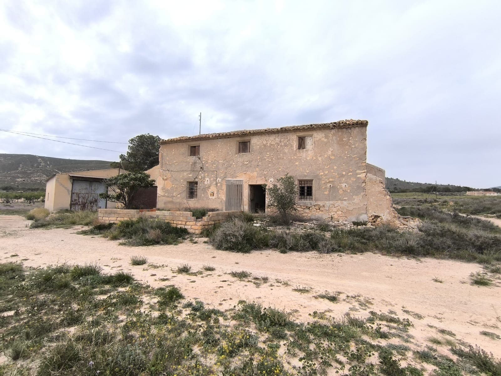 Descubra una oportunidad única para adquirir un proyecto de restauración enclavado en la serena campiña de Jumilla. Esta propiedad combina encanto rústico y potencial, ideal para quienes buscan crear la casa de sus sueños o invertir en ella. Situada a 20 km de Jumilla y a 18 km de Pinoso, esta propiedad se encuentra en una aldea remota y deshabitada, ofreciendo paz y tranquilidad. Detalles de la propiedad: Casa Antigua (213 m²): Esta casa de dos plantas cuenta con 8 amplios dormitorios, una cocina con una gran chimenea y techos altos que le aportan carácter y estilo tradicional español. Tenga en cuenta que el techo se ha derrumbado en varias zonas y la casa requiere una restauración completa. Un garaje anexo ofrece espacio adicional. Almacén (155 m²): Almacén de construcción sólida y en buen estado, que ofrece amplio espacio para almacenamiento o posible conversión. Terreno (10.800 m²): Disfrute de impresionantes vistas a la montaña desde este terreno, ideal para jardinería, agricultura o simplemente para disfrutar de la belleza natural de la zona. La parcela conserva restos de una antigua edificación. La propiedad está conectada a la red eléctrica y tiene acceso a agua potable y de riego, lo que garantiza la comodidad para el desarrollo futuro. Esta es una oportunidad única para invertir en una propiedad con un potencial inmenso en un entorno pintoresco. ¡No pierda la oportunidad de hacer realidad este proyecto de restauración! Sobre la zona: Jumilla es un encantador pueblo famoso por sus pintorescos viñedos y su vibrante cultura local. Conocido principalmente por sus vinos galardonados, este pintoresco pueblo ofrece una combinación perfecta de tradición española y modernidad. Con sus monumentos históricos, sus animadas plazas y su hermoso paisaje rural, Jumilla ofrece un entorno ideal para quienes buscan un estilo de vida tranquilo y dinámico en la provincia de Murcia, a 80 minutos de la Costa Blanca. Sobre nosotros: Contamos con una amplia cartera de propiedades en la Costa Blanca y la Costa Cálida, especializándonos en fincas, villas, fincas, terrenos edificables y opciones de diseño y construcción en las regiones de Alicante y Murcia, con especial énfasis en Elda, Monóvar, Pinoso, Sax, Villena, Aspe, Fortuna, Albacete y muchas otras zonas de los alrededores. Llevamos establecidos desde 2004 y nuestro equipo cuenta con décadas de experiencia para ayudarle a encontrar y asegurar la casa de sus sueños. Le acompañamos en cada paso del proceso para garantizar que su compra en España sea segura y sin complicaciones. No estamos aquí para venderle una propiedad, sino para ayudarle a hacer realidad su sueño y encontrar la propiedad perfecta para usted. Con nosotros, está en las mejores manos. Contáctenos ahora para hablar sin compromiso sobre cómo usted también puede hacer realidad sus sueños.