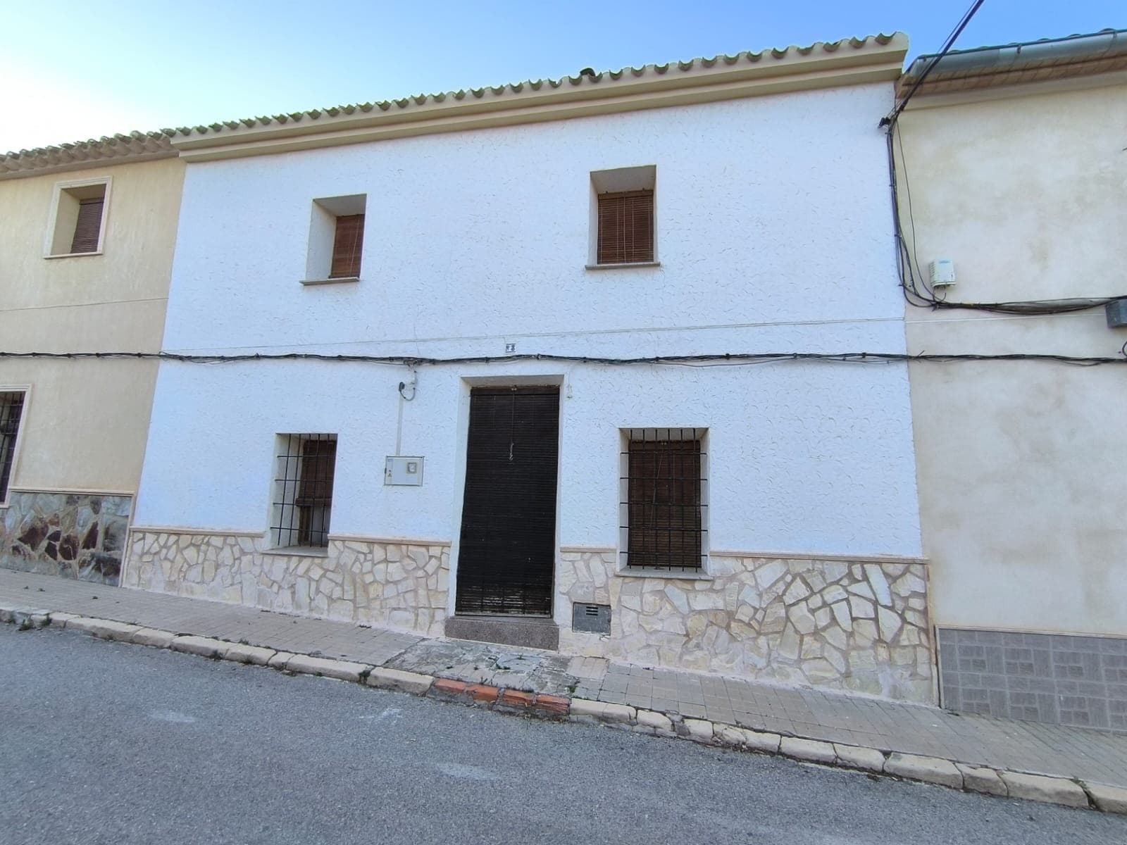 Esta casa adosada en el centro de Raspay ofrece una oportunidad única para quienes buscan invertir en una casa parcialmente terminada y convertirla en la casa de sus sueños. La propiedad cuenta con 380 m², de los cuales 280 m² están dedicados a la casa, distribuidos en dos plantas. La vivienda cuenta con 7 dormitorios, un acogedor salón con chimenea, cocina y un baño. En el exterior, encontramos un patio privado con zona de barbacoa cubierta, y la primera planta ofrece una terraza privada. Los suelos y techos son nuevos; el salón, dos dormitorios y el baño están terminados en estilo tradicional español y están listos para entrar a vivir. El resto del interior está para terminar o reformar. Frente a la casa, hay un garaje de 100 m² equipado con una estufa antigua y amplio espacio para almacenamiento u otros usos. La propiedad cuenta con conexión a los servicios básicos, como electricidad, agua potable y alcantarillado, con fibra óptica disponible en la zona. Cabe destacar que la cocina esconde un antiguo depósito de agua de lluvia debajo. Si bien esta casa requiere una renovación importante, presenta una gran oportunidad a un precio económico para aquellos dispuestos a invertir en su potencial. Sobre la zona: Enclavada en el pintoresco pueblo de Raspay, la zona ofrece fácil aparcamiento, un tranquilo ambiente rural español y amplias oportunidades para practicar senderismo y relajarse. No deje pasar la oportunidad de adquirir un trocito de paraíso a un precio muy atractivo. Sobre nosotros : Disponemos de una amplia cartera de propiedades en la Costa Blanca y la Costa Cálida, especializándonos en fincas, villas, fincas, terrenos edificables y opciones de diseño y construcción en las regiones de Alicante y Murcia, con especial énfasis en Elda, Monóvar, Pinoso, Sax, Villena, Aspe, Fortuna, Albacete y muchas otras zonas de los alrededores. Llevamos establecidos desde 2004 y nuestro equipo cuenta con décadas de experiencia para ayudarle a encontrar y asegurar la casa de sus sueños. Le acompañamos en cada paso del proceso para garantizar que su compra en España sea segura y sin complicaciones. No estamos aquí para venderle una propiedad, sino para ayudarle a hacer realidad su sueño y encontrar la propiedad perfecta para usted. Con nosotros, está en las mejores manos. Contáctenos ahora para hablar sin compromiso sobre cómo usted también puede hacer realidad sus sueños.