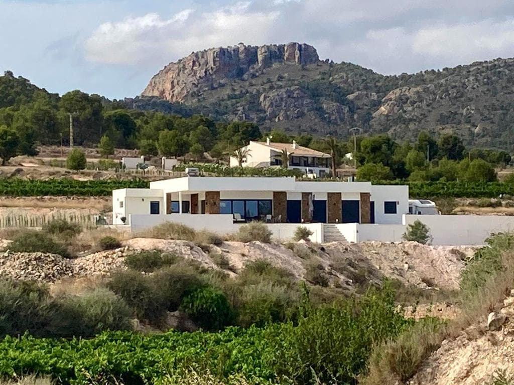Esta villa sobre plano ofrece un diseño moderno con una superficie construida de 170 m², dos dormitorios, dos baños y una luminosa cocina abierta con salón. La distribución es funcional y está diseñada para una vida cómoda durante todo el año. El precio incluye una piscina infinita privada y un garaje, así como una sala de piscina con ducha, inodoro, lavabo y espacio para la bomba de la piscina, entre otros. La casa se puede personalizar según sus necesidades. La villa se construirá en una parcela de 10.000 m², que no está incluida en el precio base. Ofrecemos una amplia selección de más de 150 parcelas legales en diversas zonas rurales. Los precios de las parcelas y el coste final pueden variar según la ubicación y las características elegidas. Este tipo de obra nueva es ideal para quienes buscan espacio, privacidad y flexibilidad, a la vez que se encuentran cerca de pueblos como Pinoso, La Romana o Monóvar. Estas zonas son conocidas por sus paisajes, viñedos y su encanto tradicional español, a la vez que se mantienen cerca de la costa y del aeropuerto de Alicante. Perfectas para vivir a tiempo completo o como refugio vacacional. Disponemos de una amplia cartera de propiedades en la Costa Blanca y la Costa Cálida, especializándonos en fincas rústicas, villas, fincas, terrenos edificables y opciones de diseño y construcción en las regiones de Alicante y Murcia, con especial énfasis en Elda, Monóvar, Pinoso, Sax, Villena, Aspe, Fortuna, Albacete y muchas otras zonas de los alrededores. Llevamos establecidos desde 2004 y nuestro equipo cuenta con décadas de experiencia para ayudarle a encontrar y asegurar la casa de sus sueños. Le acompañamos en cada paso del proceso para garantizar que su compra en España sea segura y sin complicaciones. No estamos aquí para venderle una propiedad, sino para ayudarle a hacer realidad su sueño y encontrar la propiedad perfecta para usted. Con nosotros, está en las mejores manos. Contáctenos ahora para hablar sin compromiso sobre cómo usted también puede hacer realidad sus sueños.
